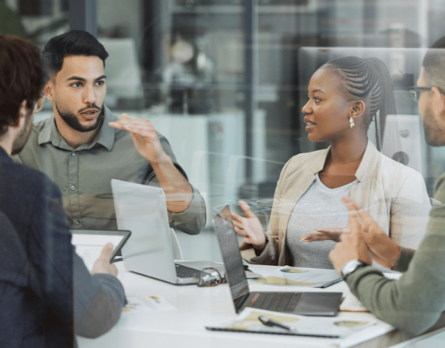 Three males and one female sat around an office desk discussing a project