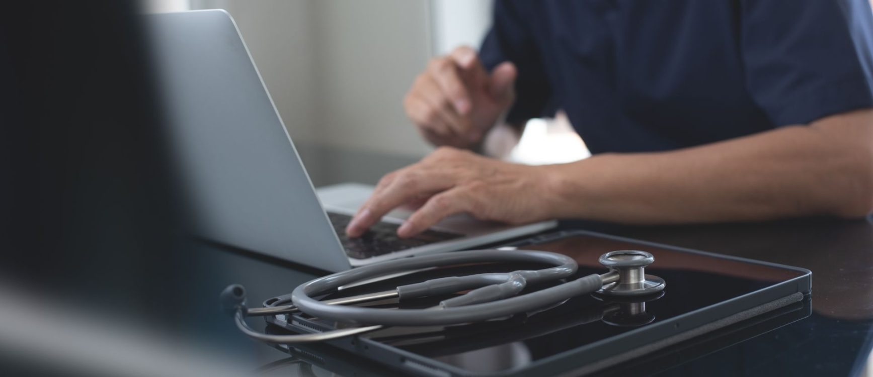Close up shot of medical professional on a laptop; medical equipment in foreground.