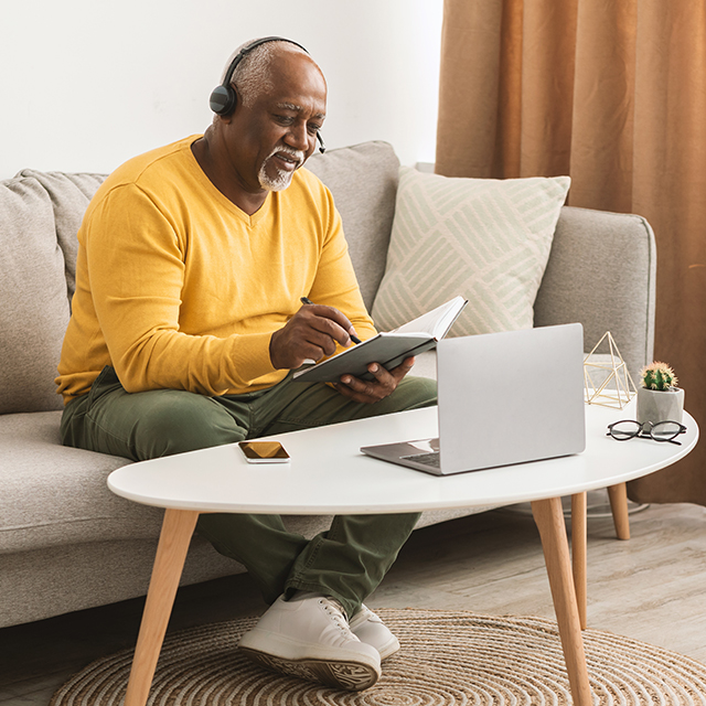 Senior African American Man Using Laptop Taking Notes At Home
