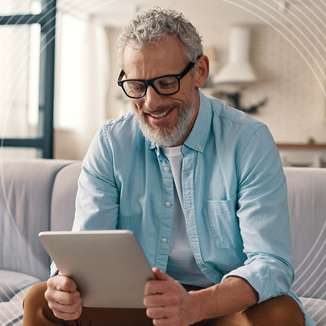 Nest Pension Services images - Cheerful senior man in casual clothing using digital tablet while sitting on the sofa at home