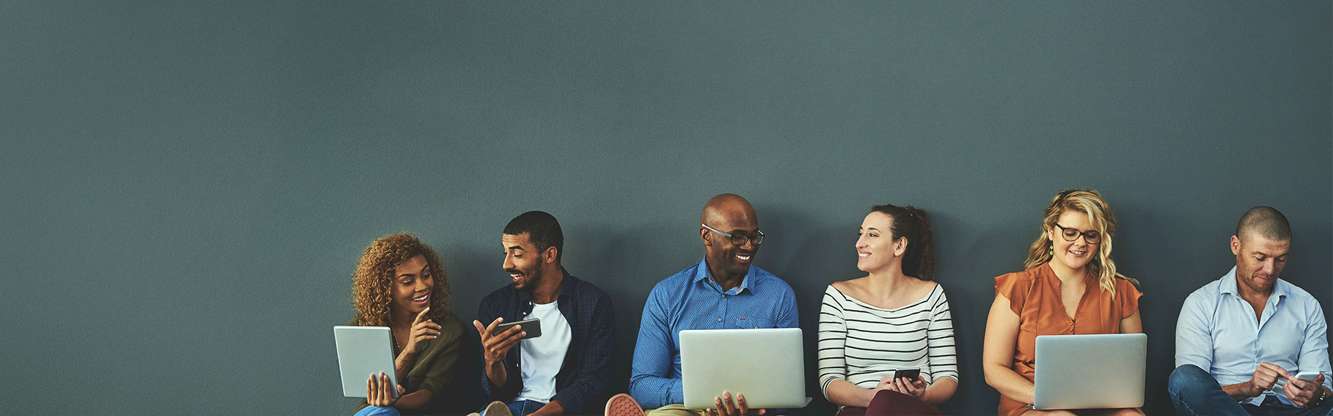 Group of happy business people sharing information on wireless technology in a row at an office together.